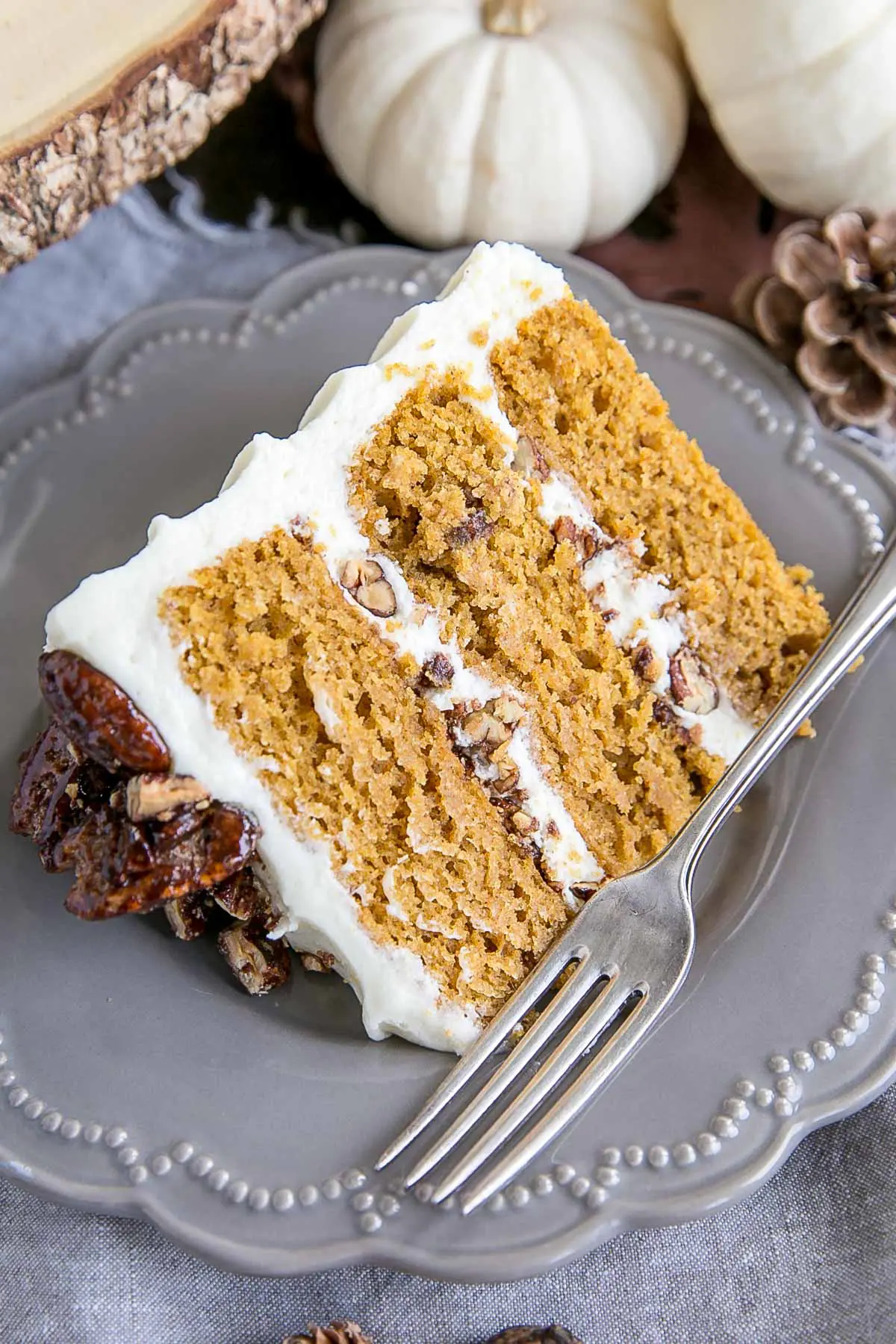 Slice of cake on a plate. Three layers of cake with candied pecans and cream cheese frosting.