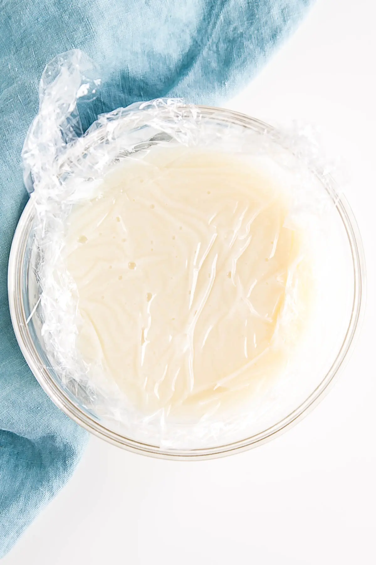 Flour mixture in a glass bowl with plastic wrap directly on top of it.