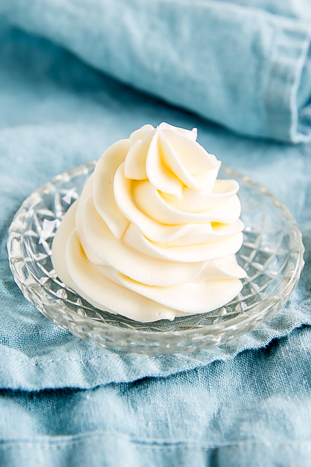 Angled photo of a piped buttercream swirl on a small glass plate.