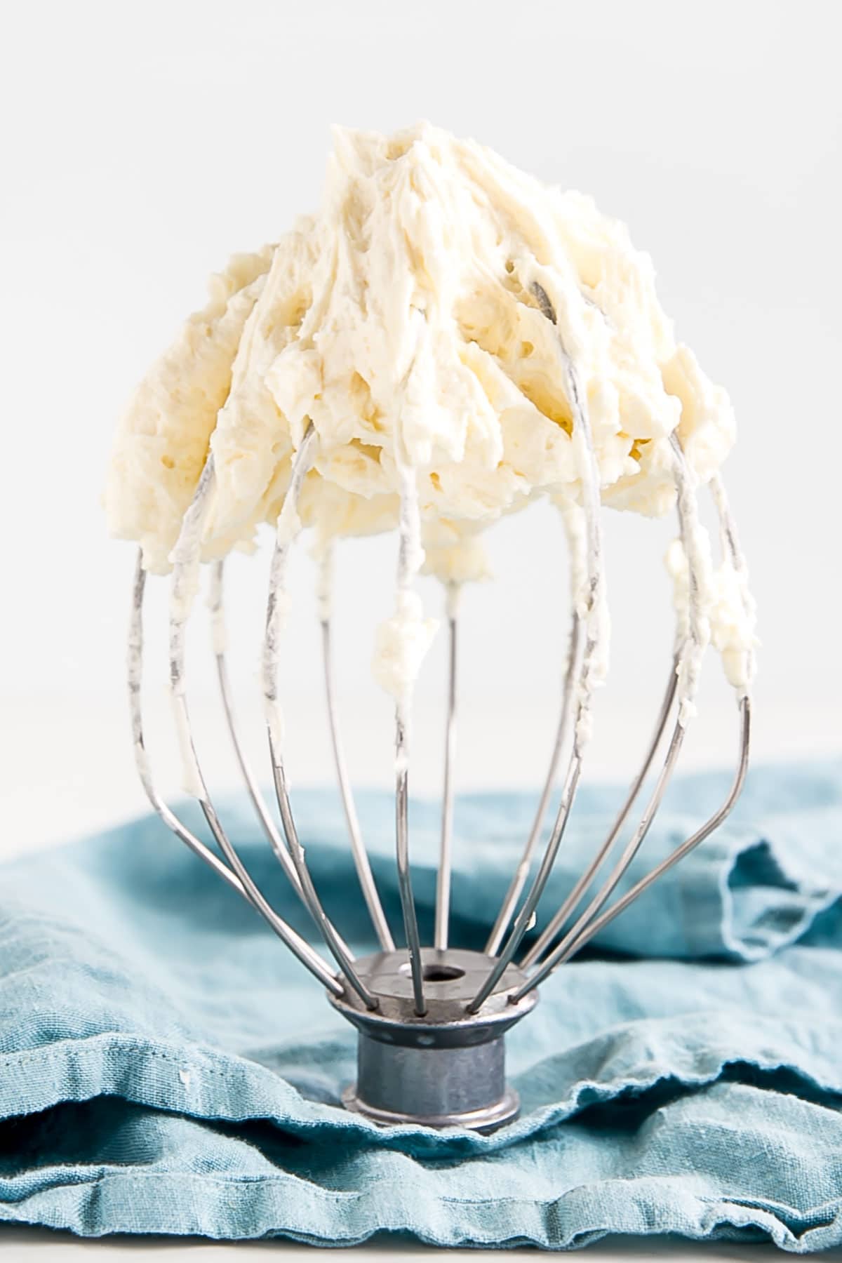 Ermine Frosting on a stand mixer whisk with a blue cloth in the background.