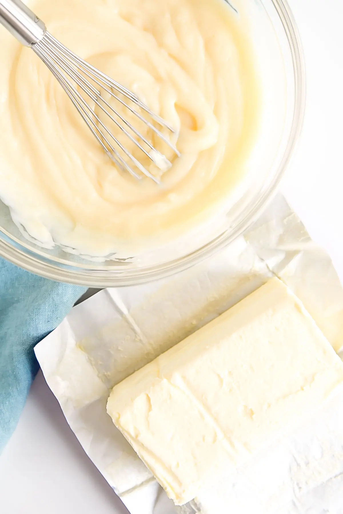 Pastry cream in a bowl with a whisk and butter next to it.