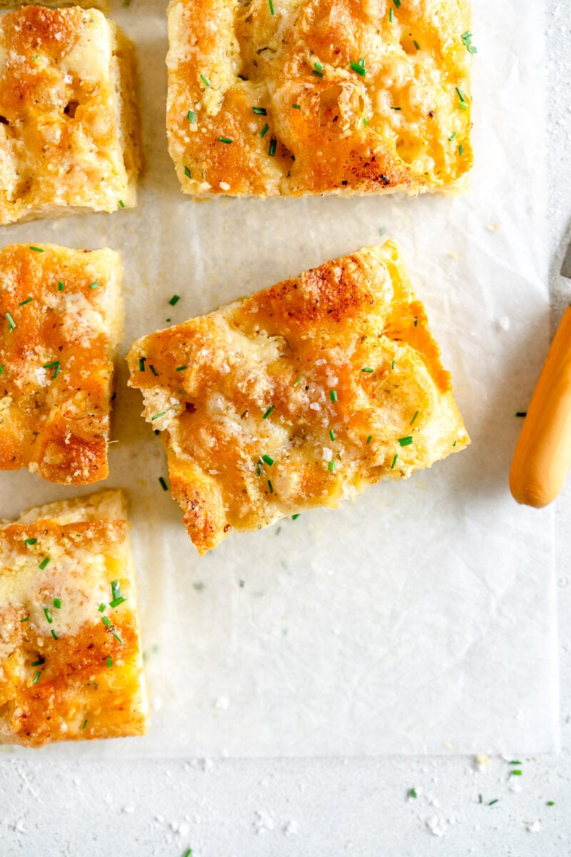 piece of baked cheesy garlic bread on paper surrounded by other pieces of bread